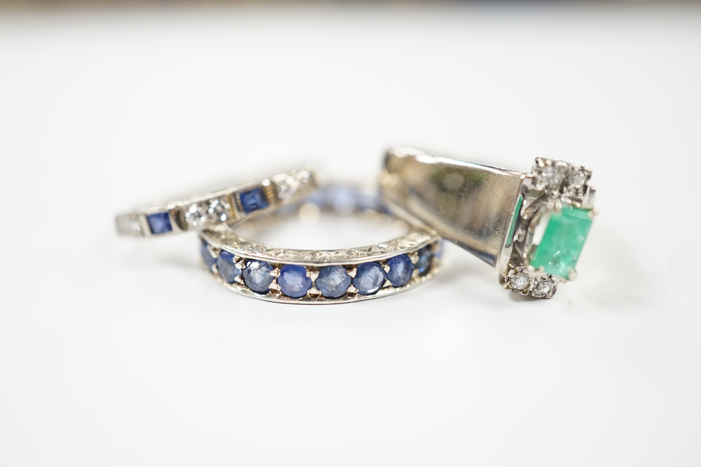 An 18k white metal, emerald and diamond set dress ring, size O, a white metal and sapphire set full eternity ring (stones missing) and an 18ct, sapphire and diamond set half hoop ring, gross weight 10 grams.